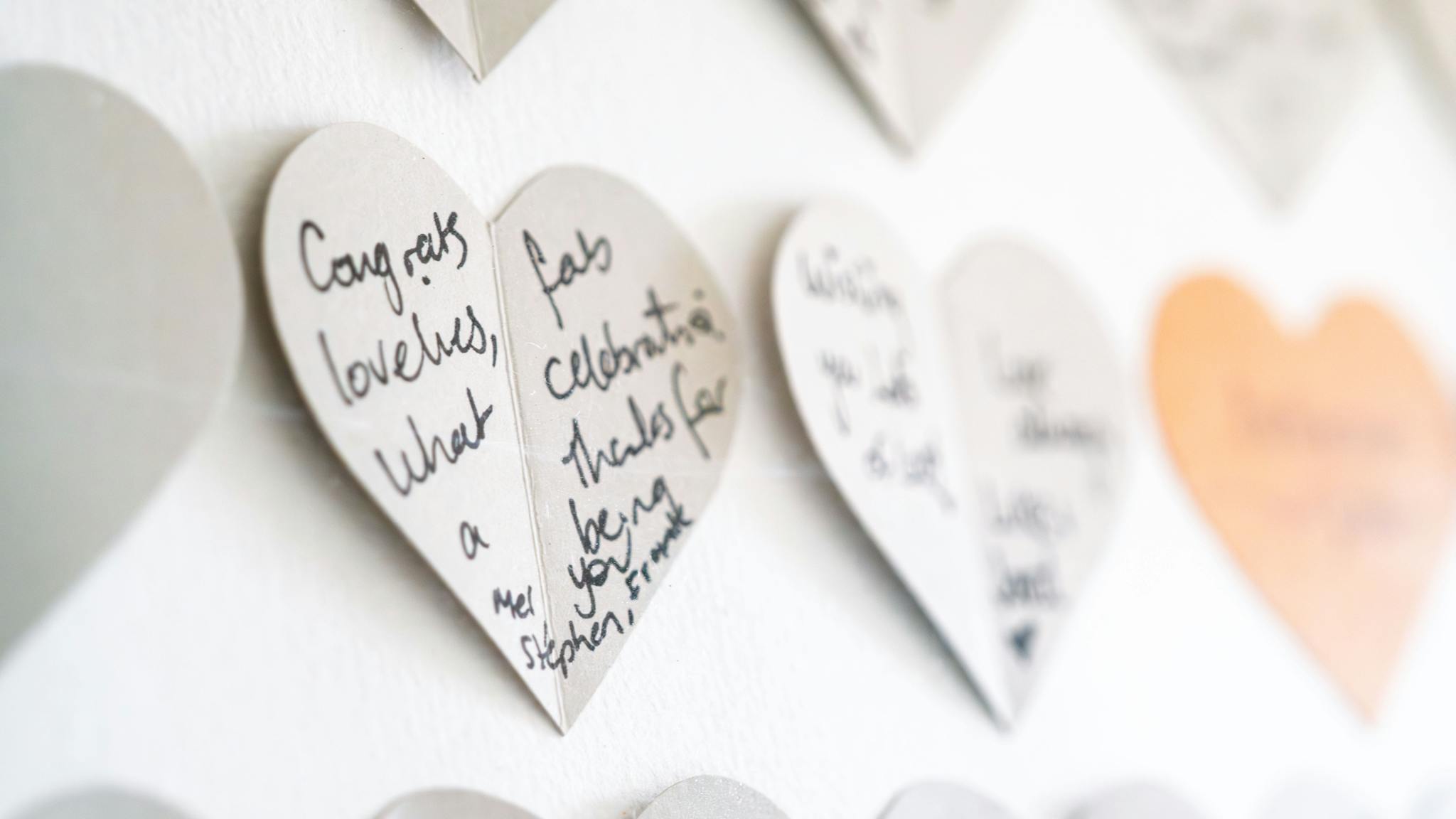 Close-up view of heart-shaped cards with handwritten congratulatory messages on a wall.