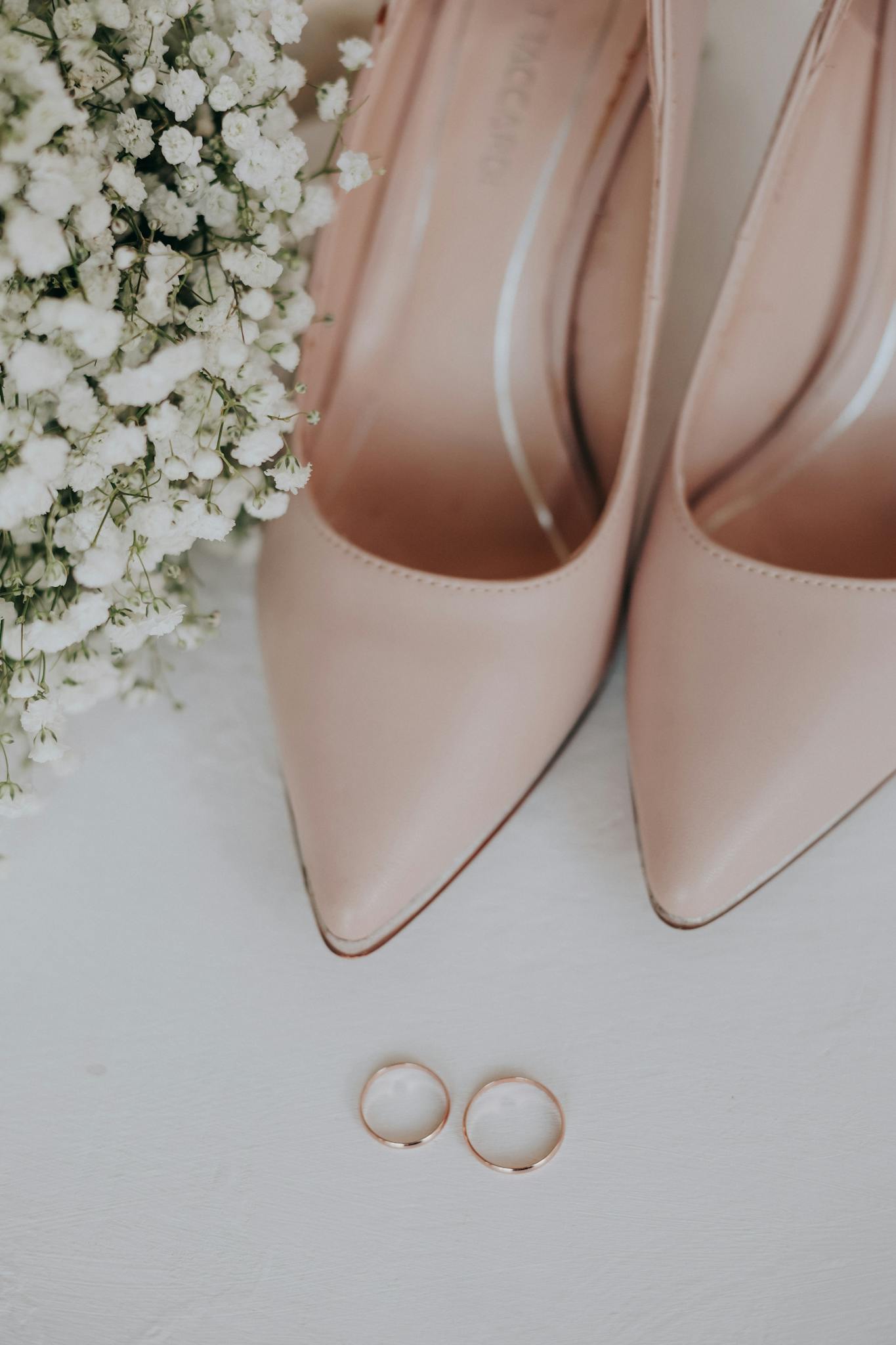 Flat lay of pink shoes, elegant bouquet, and wedding rings on a white background.